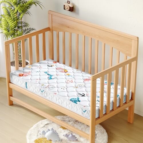 Wooden baby crib with a colorful mattress and a plant nearby.